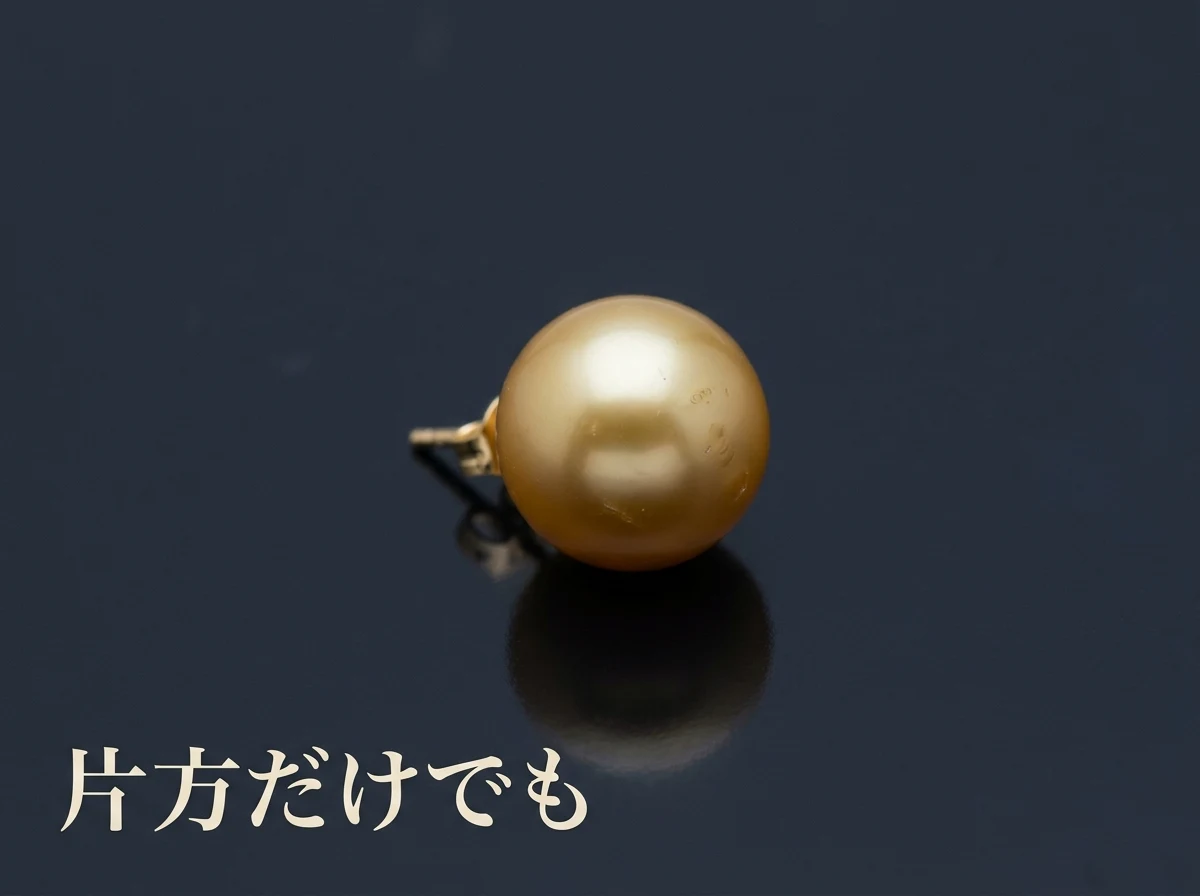 片方だけの金色の真珠のピアスを暗い面に置いた写真