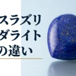 光沢のある面に置いた、金色の粒が散る濃い青のラピスラズリをハート形に磨いた石の写真。画像内の文字は「ラピスラズリ」「ソーダライト」「2つの違い」